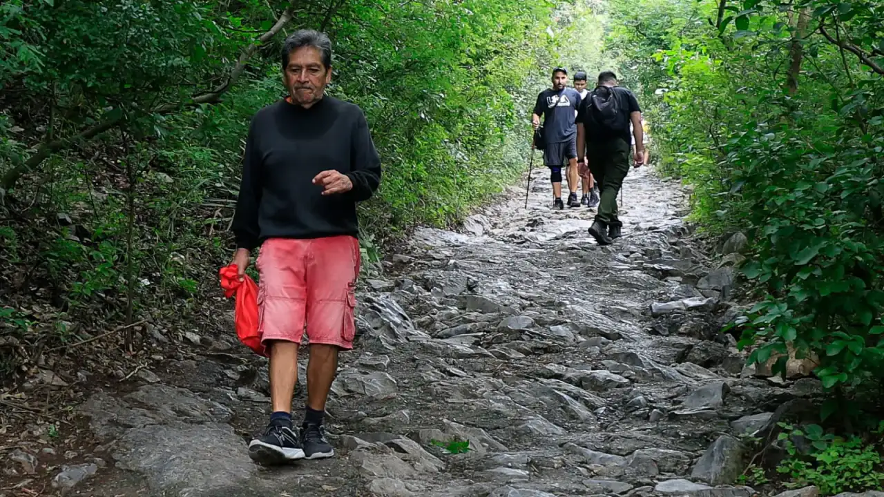 Personas caminando por sendero en el Cerro de la Silla con gorras y mochilas