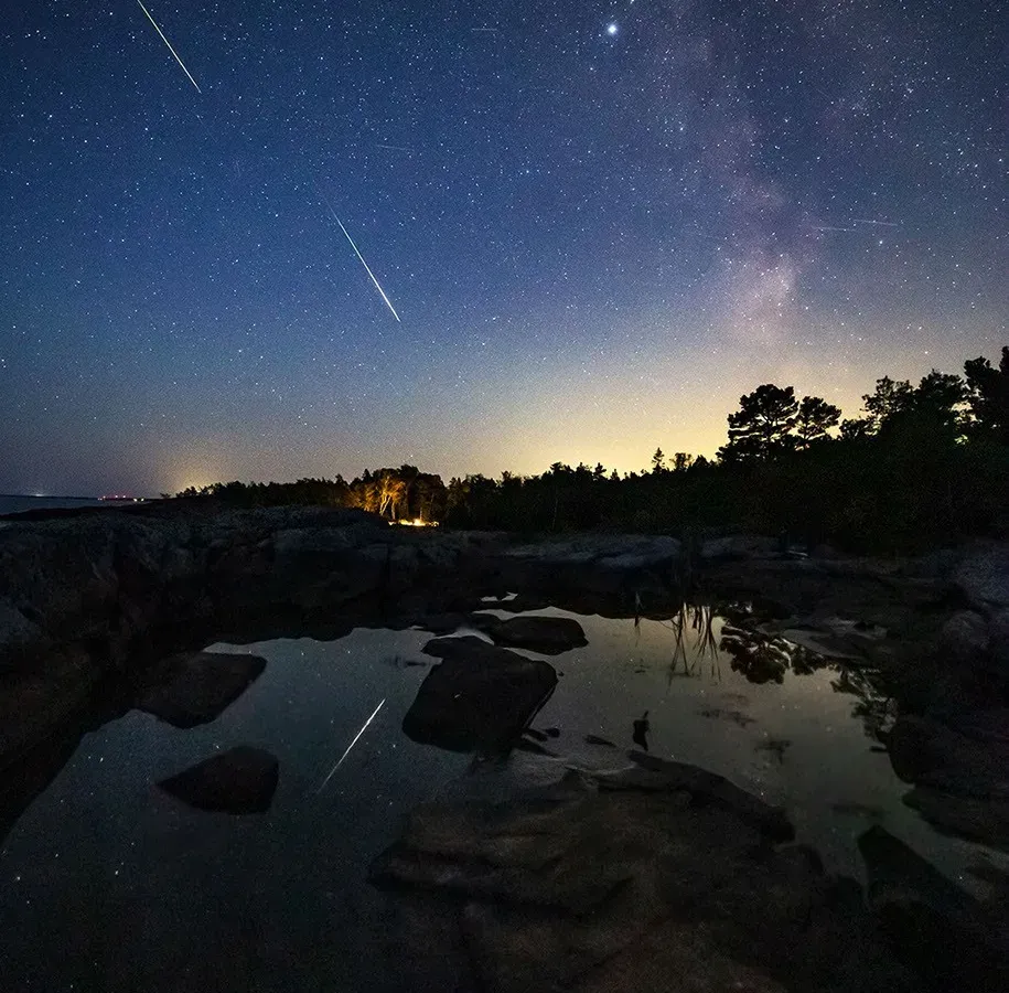 Dos meteoros brillantes sobre un paisaje costero en Suecia, con la Vía Láctea de fondo.