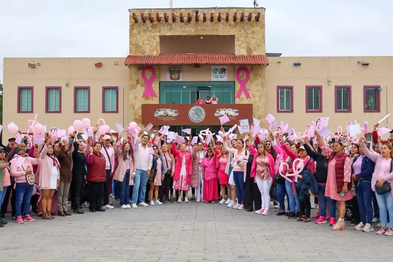 Mujeres y autoridades durante una caminata y formación de un moño rosa en la plaza principal