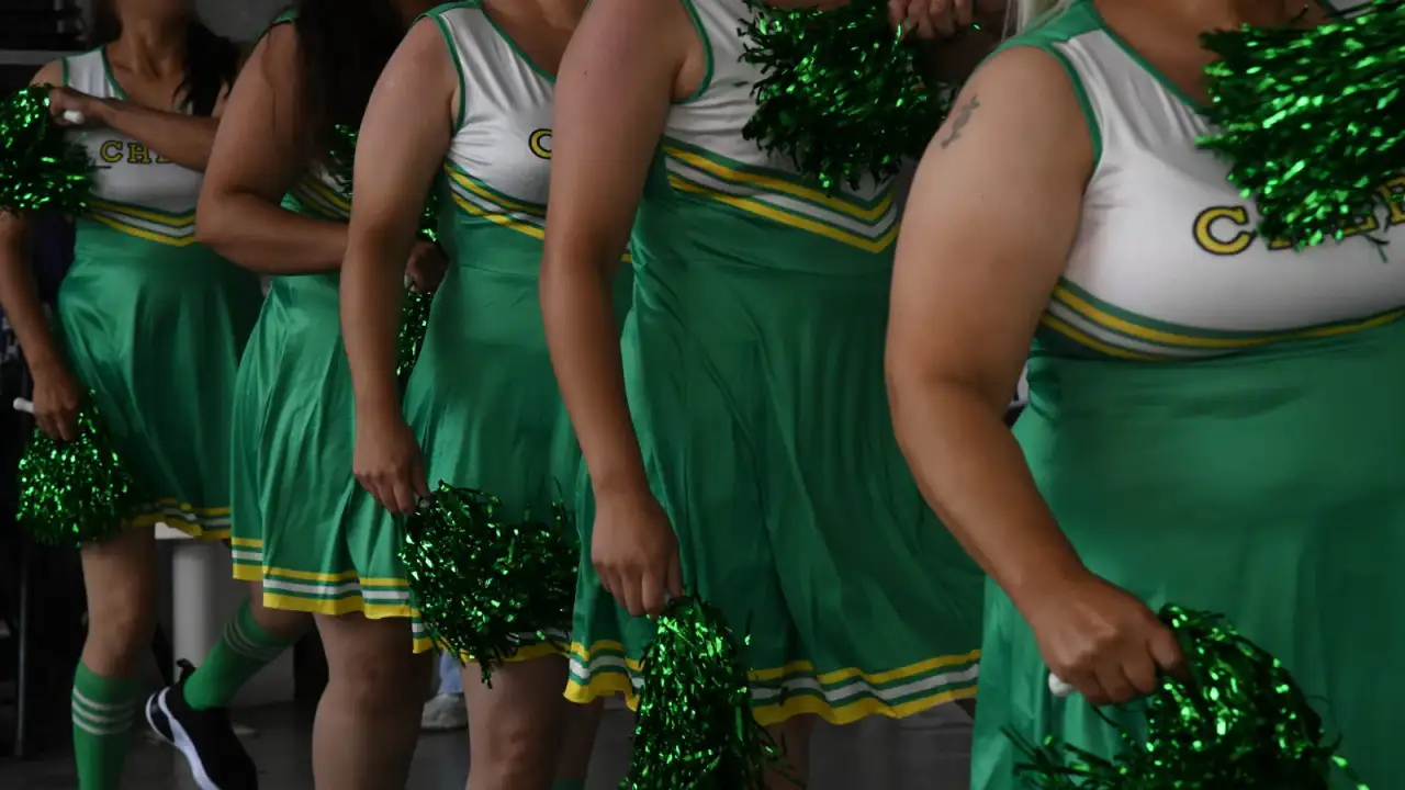 Mujeres en uniforme de porristas con pompones verdes y amarillos dentro de un centro penitenciario en León, Guanajuato.