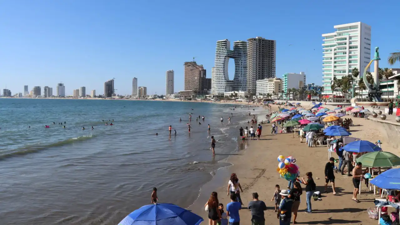 Vista panorámica de la playa de Mazatlán con turistas y hoteles al fondo