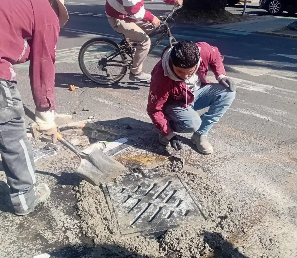 Trabajadores limpiando una coladera en una calle de Toluca