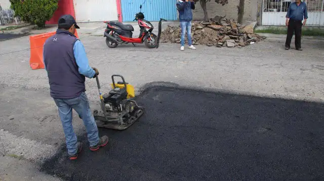Maquinaria y trabajadores realizando labores de bacheo en una vialidad urbana