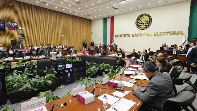 Sala de sesiones del Consejo General del INE con consejeros en pantalla y presídium