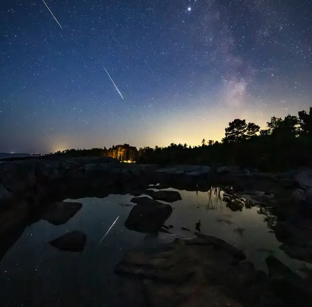 Dos meteoros brillantes sobre un paisaje costero en Suecia, con la Vía Láctea de fondo.