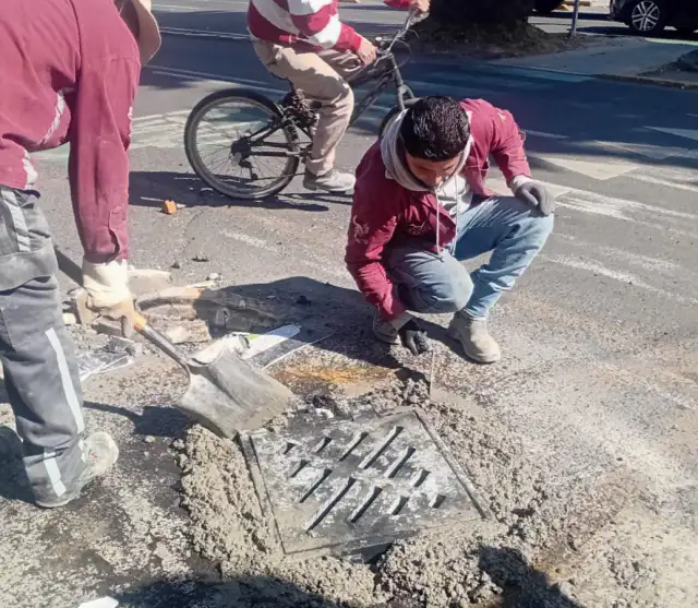 Trabajadores limpiando una coladera en una calle de Toluca