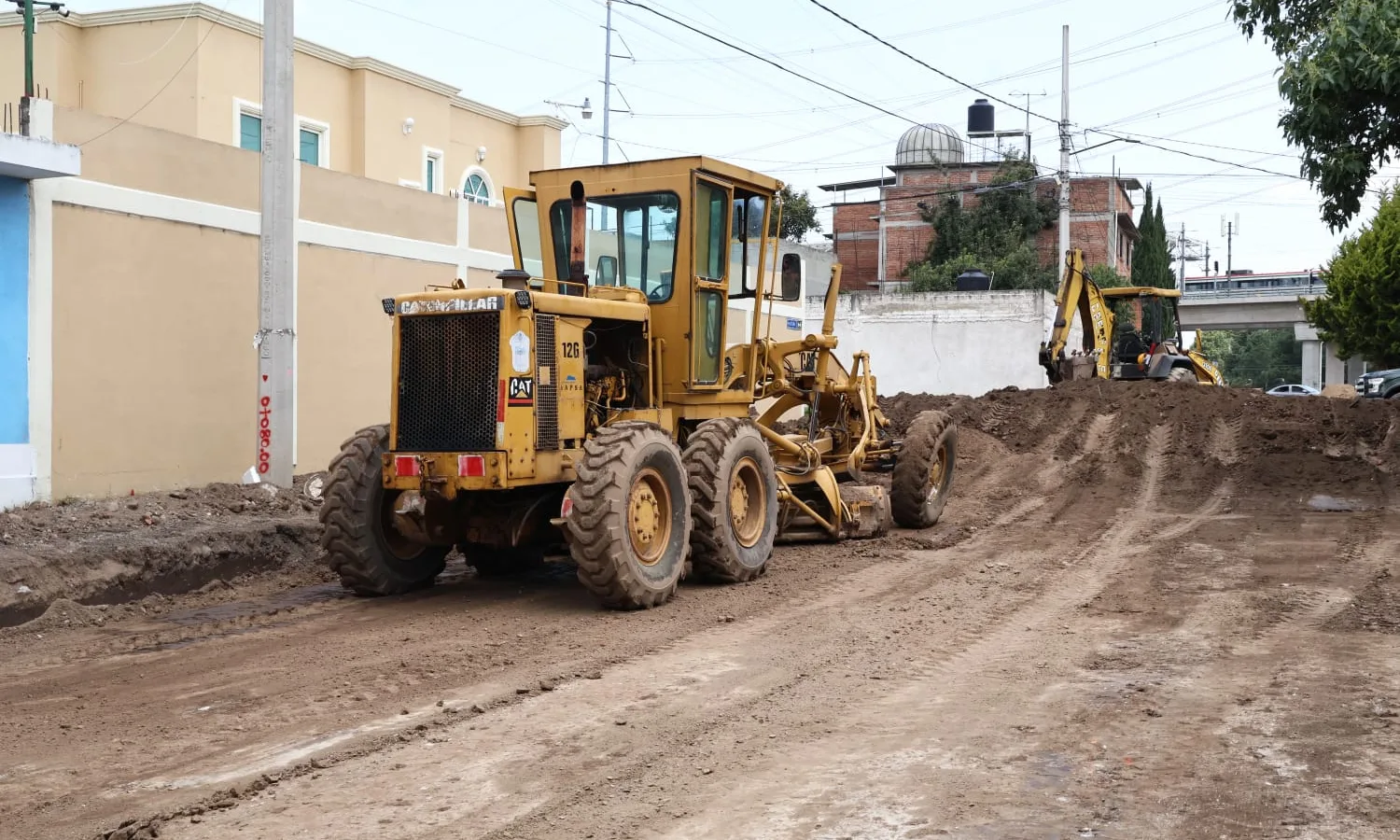 Obras de pavimentación en una calle de Toluca con maquinaria y trabajadores.